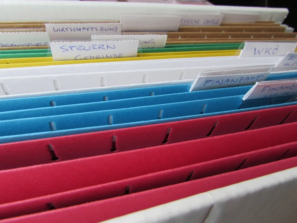 Pastas suspensas coloridas com etiquetas escritas à mão em uma gaveta de arquivo
